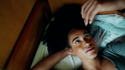 One pensive young black latina lying in bed with thoughtful contemplative expression gazing at...