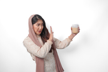 A serious young Asian Muslim woman wearing veil hijab gesturing rejection to a cup of coffee on...
