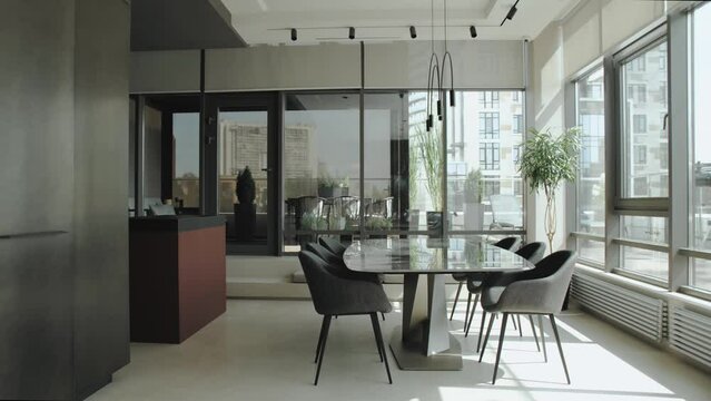Dining room kitchen interior in luxury modern apartment, big marble table with chairs and large window on background, slow motion.