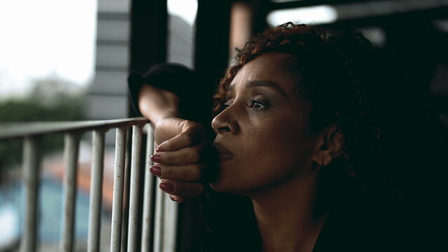 One sad pensive black middle-aged woman gazing at view from balcony in deep melancholic contemplation. Close-up face of an African American lady feeling lost in thought, pondering life's challenges - Powered by Adobe