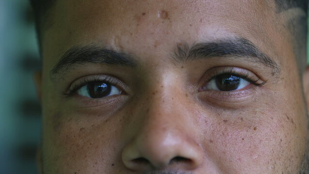One serious young black latin hispanic man close-up eyes staring at camera with solemn expression. South American Brazilian person eye to eye stare
