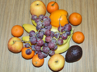 fruits on a wooden background - clementines, persimmon, apples, apple, bananas, avocado, pink grapes