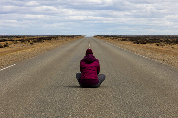 Pessoa sentada na rodovia olhando o horizonte