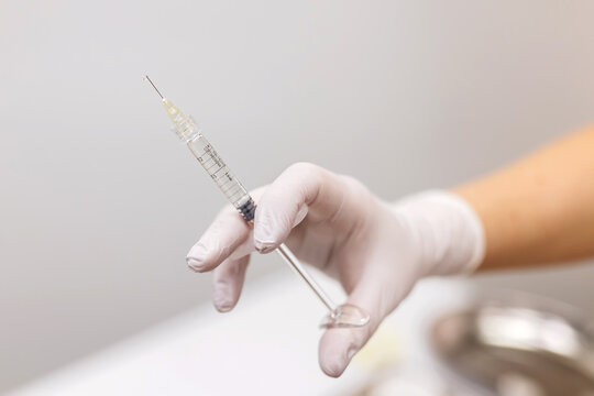 A female cosmetologist in white gloves prepares a syringe for an injection cosmetology procedure with a young woman patient. Cosmetological injections, anti-aging, cosmetologist services.