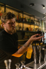 Bartender meticulously pours concentrated citrus juice from jigger into shaker. Young man measures...