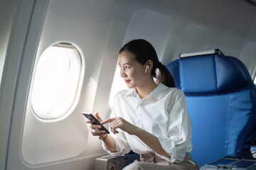 A woman is sitting on an airplane with her phone in her hand