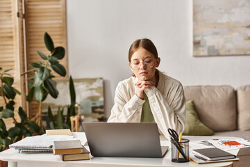 teenager girl in glasses looking at her laptop during online class at home, e-learning concept
