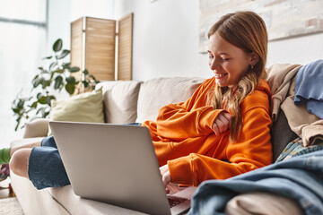 happy teenager girl watching comedy movie on a laptop while relaxing on a sofa in living room