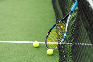 Tennis racket and tennis ball besides the net on outdoor tennis court.