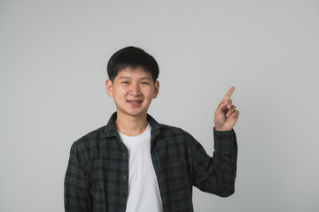 Confident Teen Man Boy with Braces Pointing Upwards. Smiling Asian teenager in checkered shirt...