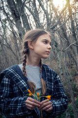Beautiful caucasian girl with braids holding a bouquet of yellow crocuses at the background of a spring forest.