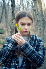 Beautiful caucasian girl with braids holding a bouquet of yellow crocuses at the background of a spring forest. - 752346747