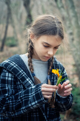 Beautiful caucasian girl with braids holding a bouquet of yellow crocuses at the background of a spring forest.