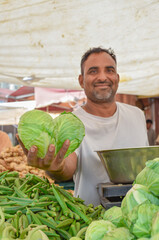 Fototapeta premium Seller showing to camera different vegetables on his hand in street market India