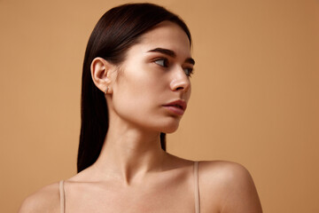 Naklejka premium Close up photo of young beautiful female woman with bare shoulders looking away against sandy color studio background. Concept of beauty, spa procedures, dermatology treatments, cosmetology care.