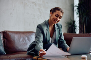 Happy businesswoman analyzing reports during conference call in hotel lobby.