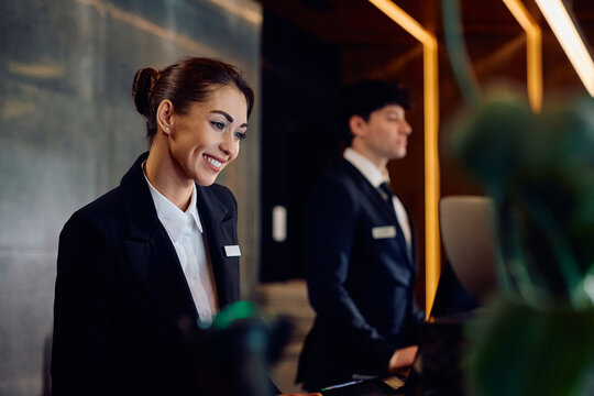 Happy female receptionist working at hotel front desk.