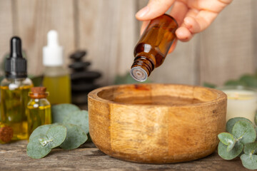 Eucalyptus essential oil in a glass bottle with green eucalyptus leaves on a textured wooden...