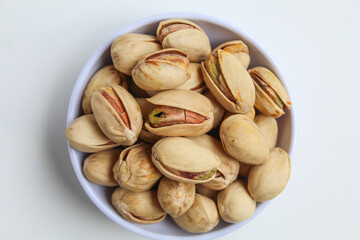 Salted pistachio on the small white bowl, isolated on white background, flat lay or top view