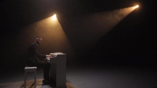 Side view with copy space on male compositor dressed in elegant wear making improvisation of melody on piano. Man sitting at musical instrument and playing beautiful song on stage lit with soft light.