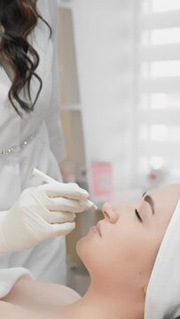 A young woman is lying on a couch in the office beautician who is performing botulinum injection procedure to reduce wrinkles around eyes and on face. Beautician makes markings on face for injections