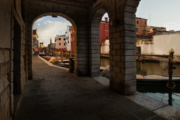 Typical view of Chioggia - hidden walkway under the arcades, beautiful ancient Italian architecture, walkway over the water canal, romantic city view, urban landscape.