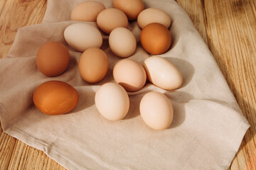Chicken eggs of different brown and beige shades on a wooden background on grey kitchen towel. Easter background. Top view
