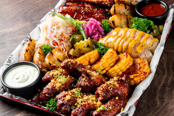 platter of assorted BBQ dishes, including ribs, grilled corn, and sausages, served with sauces and...