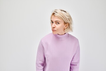 Confused young woman in a purple sweater, making a puzzled expression on a light gray background.