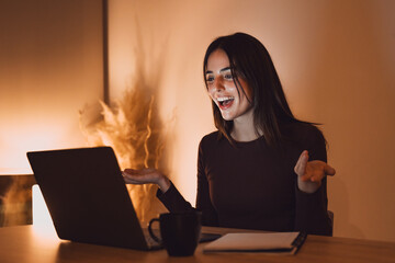 Happy millennial Caucasian woman in earphones sit at desk at home office work distant on computer....