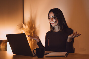 Happy millennial Caucasian woman in earphones sit at desk at home office work distant on computer....