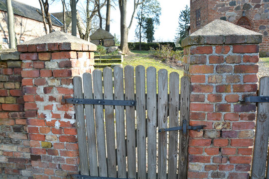 Holzt&uuml;r mit Pfosten aus Stein vor einer historischen Dorfkirche