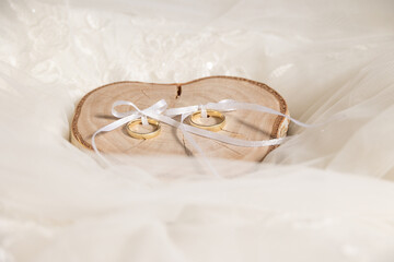 wedding rings on wood plate on tulle and wedding dress