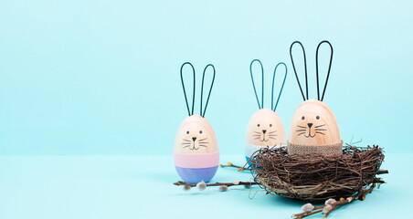 Easter bunny or rabbit sitting in a bird nest, willow branches, wooden egg, spring holiday, blue...