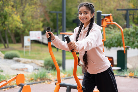 Young indian woman exercising on orbitrek machine at urban sports ground, showcasing dedication to fitness and healthy lifestyle in vibrant urban setting.
