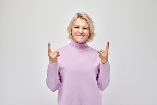 Woman in purple sweater smiling and making finger guns gesture against a white background.
