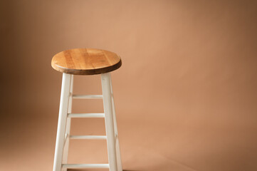 One stool or chair with wooden seat and white legs isolated on a beige backdrop with copy space