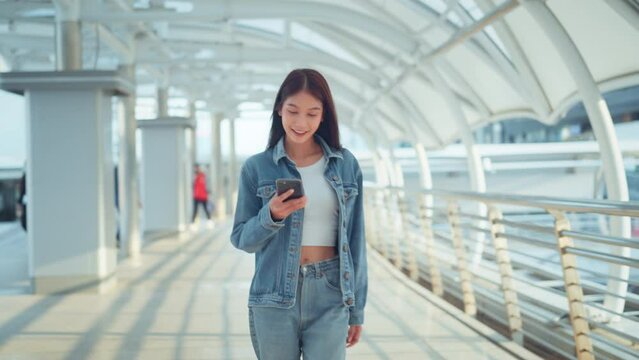 Happy young asian woman using mobile phone with chatting online with friends, Female in jean jacket walking in the city using social media on smartphone, Technology