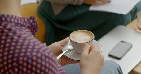 Cafe visitor holds a cappuccino, a beloved coffee beverage known for its creamy foam topping. Warm...