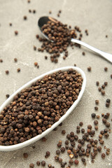 Black pepper corns in white plate on grey concrete background. Vertical photo