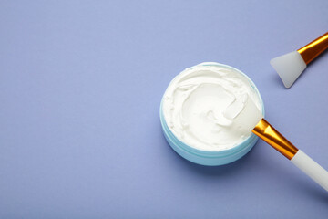 Cosmetic mask (scrub) in a bowl with brush on purple background.