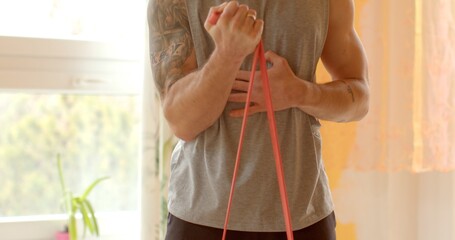 Man is engaging in home workouts, use of resistance bands for physical exercises. Bicep curls are...