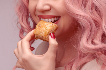 Woman with pink curly hair is eating baklava.