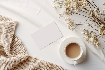 A white card with a flower on it sits on a table next to a cup of tea and a blanket mockup - Powered by Adobe
