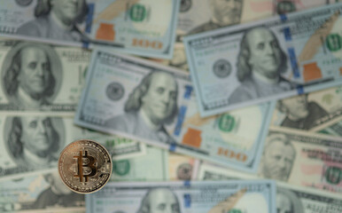 Bitcoin gold coin against the defocused background of dollar bills.