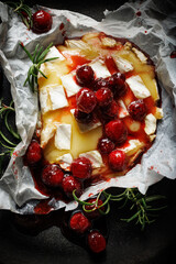Melted baked Camembert cheese with cranberry sauce and fresh rosemary on a black background, top view