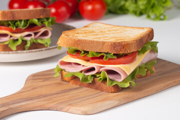 Close-up of two sandwiches with bacon, salami, prosciutto and fresh vegetables on rustic wooden cutting board. Club sandwich concept - 752430704