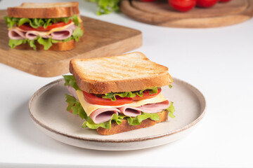 Close-up of two sandwiches with bacon, salami, prosciutto and fresh vegetables on rustic wooden cutting board. Club sandwich concept - 752430797