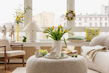 Interior design of spring living room with design sofa, furniture, vase with tulips, easter decorations, pillows and personal accessories. Home decor. Template. Easter holidays.	
