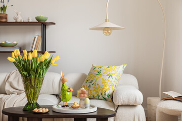Sunny and design interior of living room with easter decorations, tulips, modular sofa, shelf, pillows and elegant accessories. Home decor. Easter holidays.	
